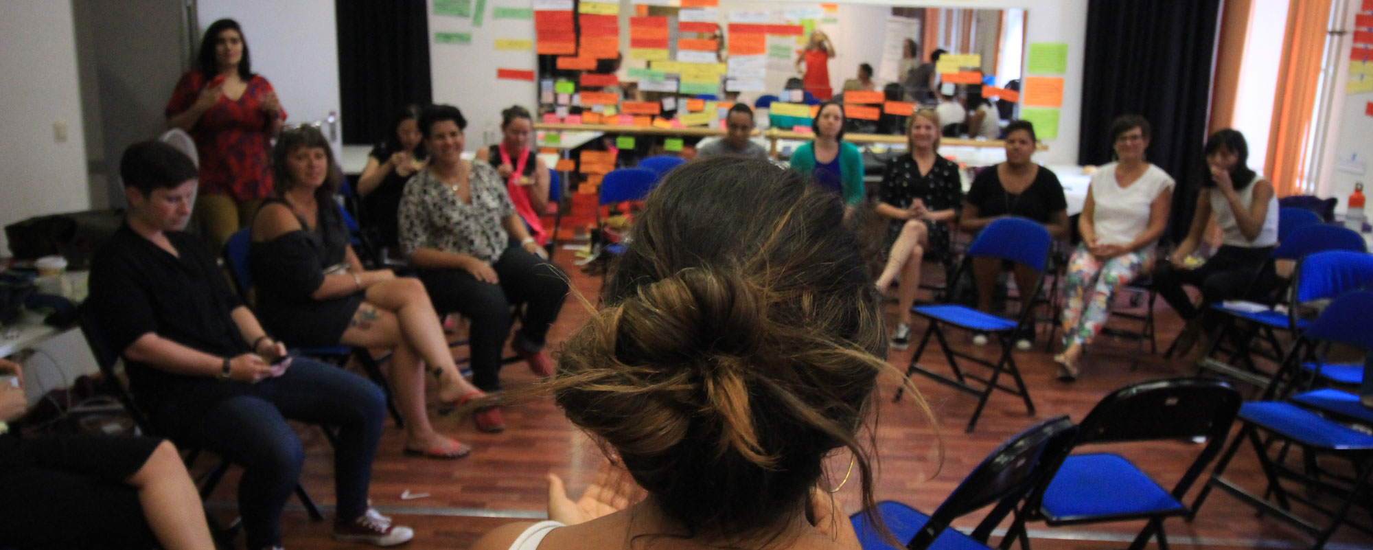 La photo montre un auditorium avec une première rangée de personnes assises dans des fauteuils roulants ayant toutes les mains levées, quelques-unes sont sur des chaises dans le coin de la photo et d’autres sont en train d’applaudir. Pre-Forum Learning Journey